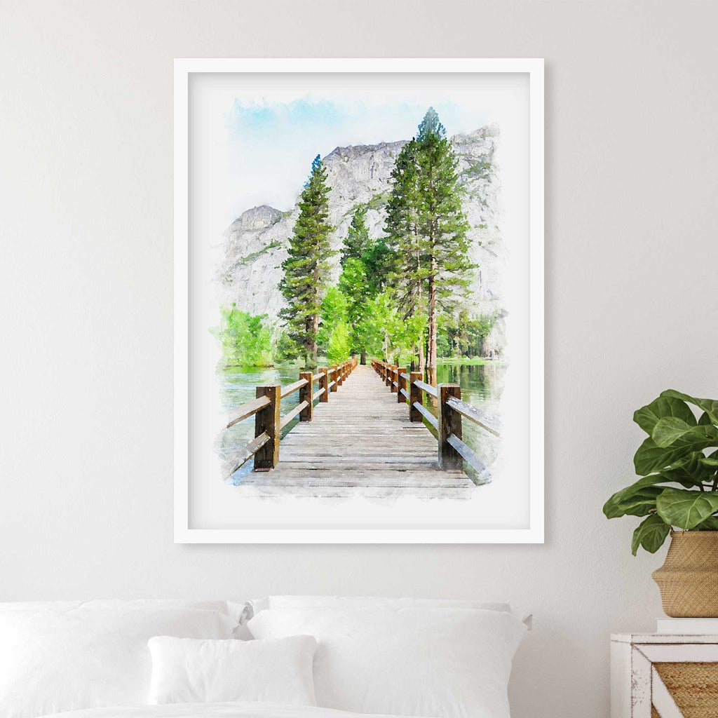 Watercolor-style portrait of a wooden footbridge leading to pine trees and a rock cliff, in a white frame above a bed