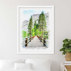 Watercolor-style portrait of a wooden footbridge leading to pine trees and a rock cliff, in a white frame above a bed