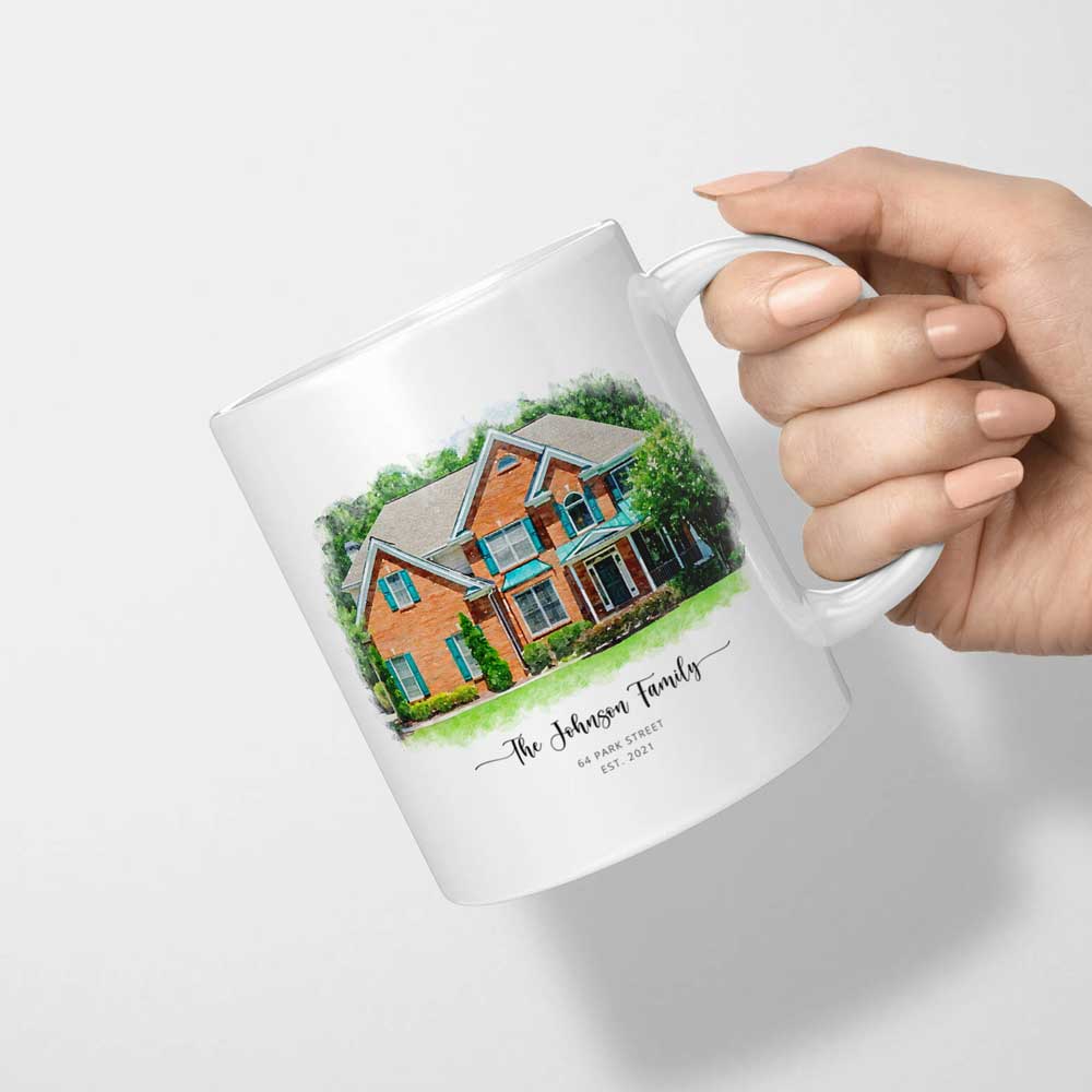 White mug tilted in a hand, printed with a watercolor-style portrait of a red brick house and 'The Johnson Family'