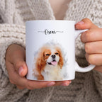 Two hands in a knit sweater hold a white mug printed with a watercolor-style portrait of a dog named 'Oscar'